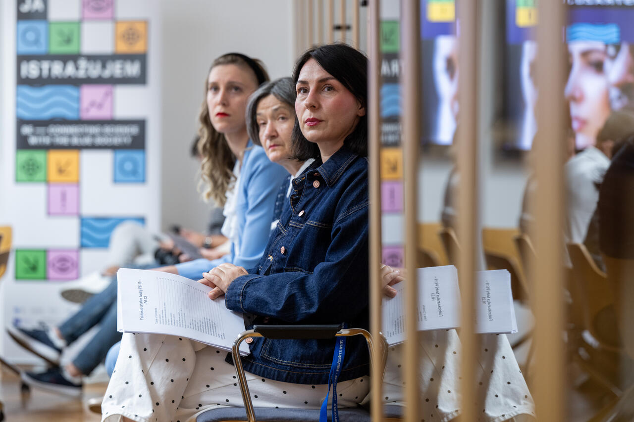 Attendees holding printed materials follow the presentation, with the European Researchers’ Night banner behind them.
