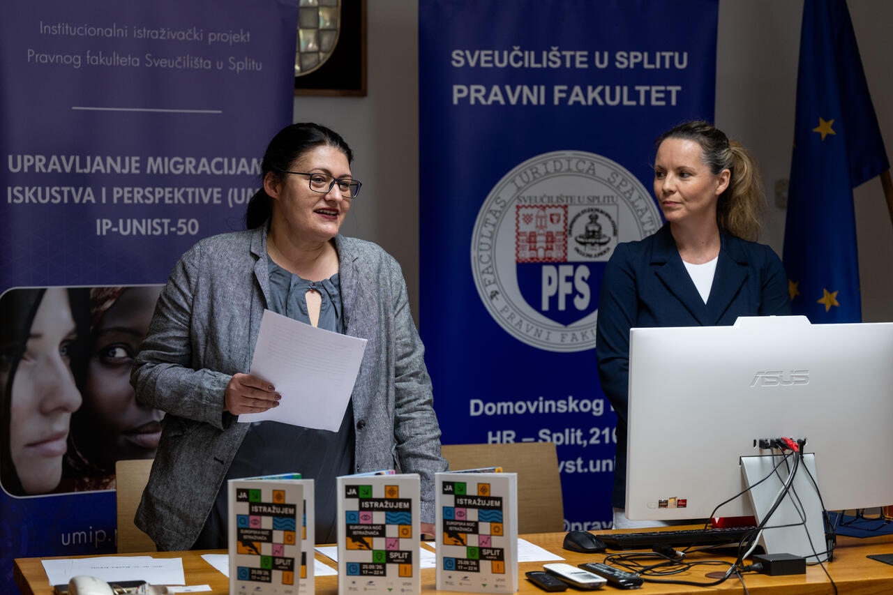 Two project members at the presentation desk between the UMIP and Faculty of Law banners, with European Researchers’ Night brochures on the desk.