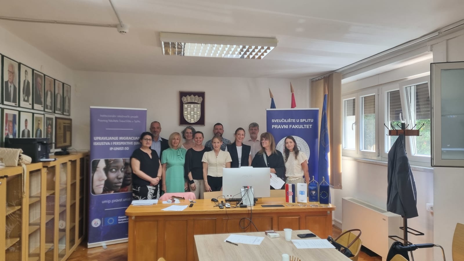 Group photo of round table participants standing between the UMIP project banner and the Faculty of Law banner in the Council Chamber.
