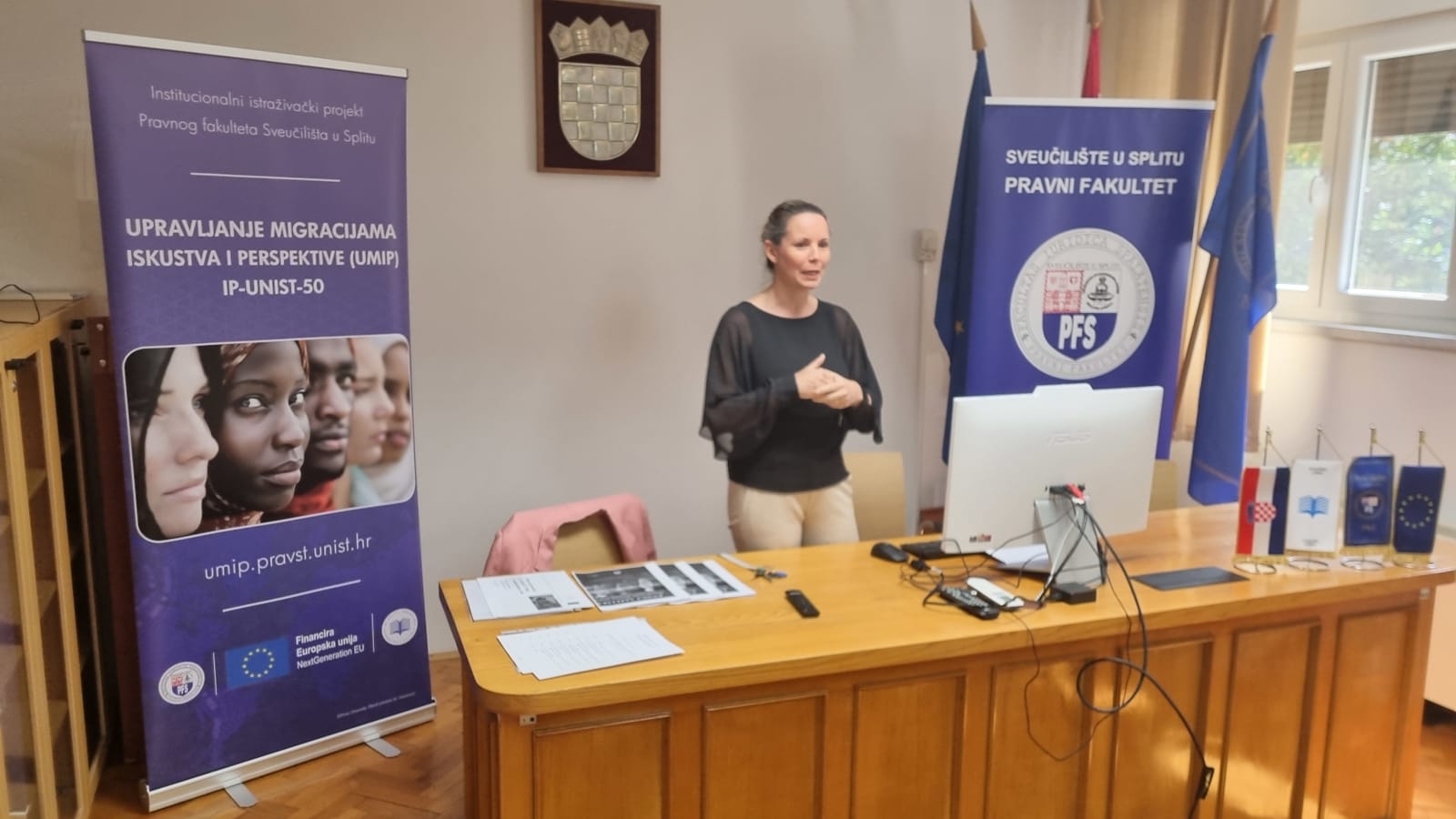 A speaker delivers a presentation behind the council desk between the UMIP and Faculty of Law banners.